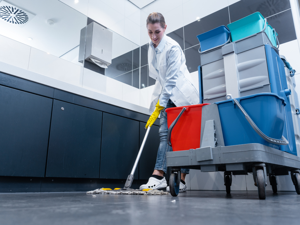 A person in a white uniform and yellow gloves mops a floor next to a cleaning cart, a key consideration when choosing a commercial cleaning company in Marietta.
