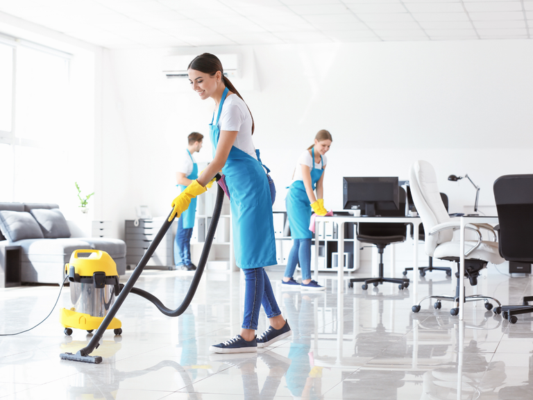 Three cleaners in blue aprons and yellow gloves clean an office, illustrating a guide on how to choose a commercial cleaning company in Marietta.