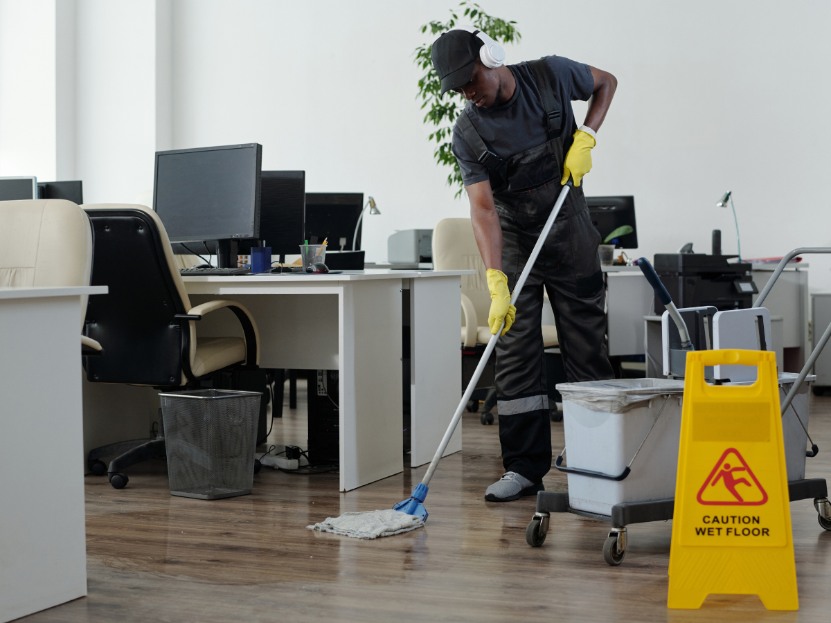 A custodian in uniform and headphones mops the floor near a yellow sign, a common sight when evaluating office cleaning cost in Marietta.